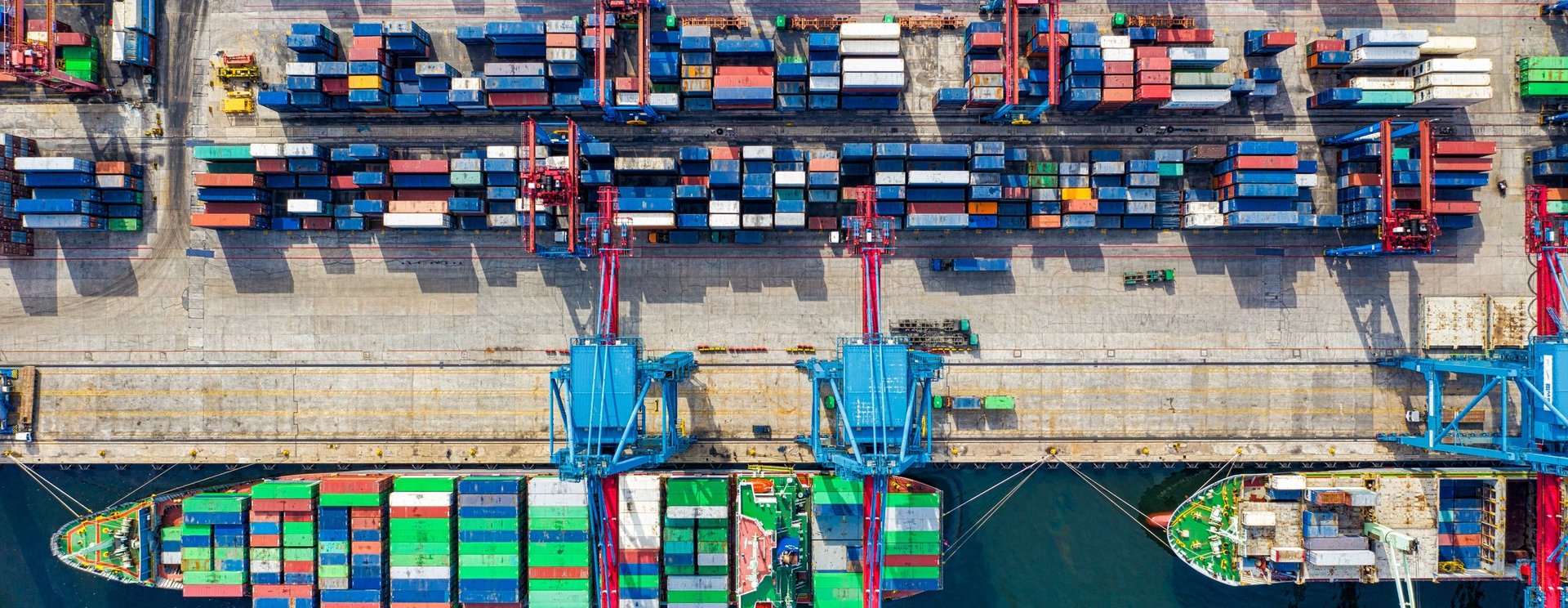 Containertermin mit einem angelegten Frachtschiff und gestapelten Frachtcontainern