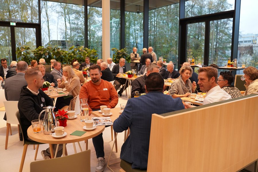 Ein großes Publikum sitzt in einer modernen Eventlocation und tauscht sich untereinander aus.