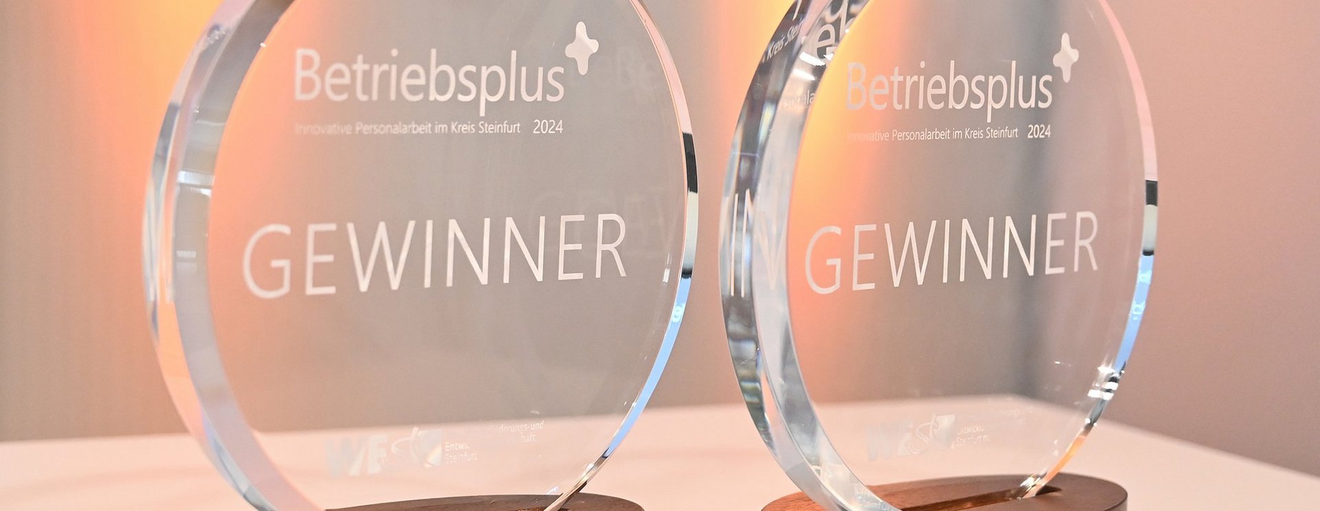 Zwei gläserne, runde Trophäen mit dem eingravierten Wort "Gewinner" stehen auf einem Tisch.