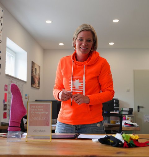 Eine Frau steht in einem Büro und lächelt in die Kamera.