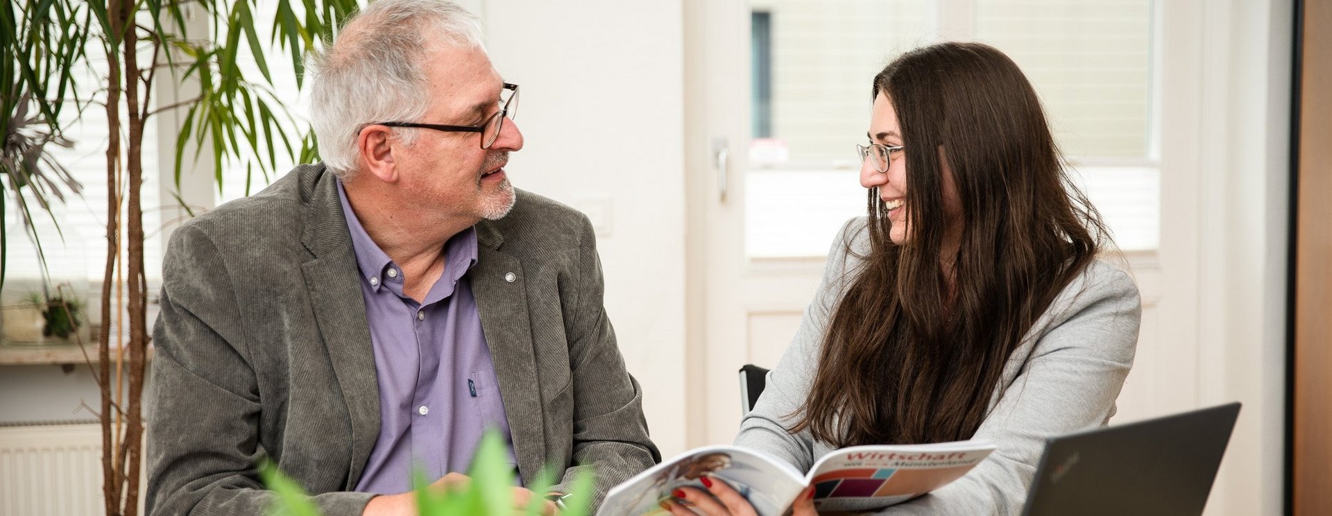 Zwei Personen sitzen an einem Tisch und schauen gemeinsam in ein Magazin.