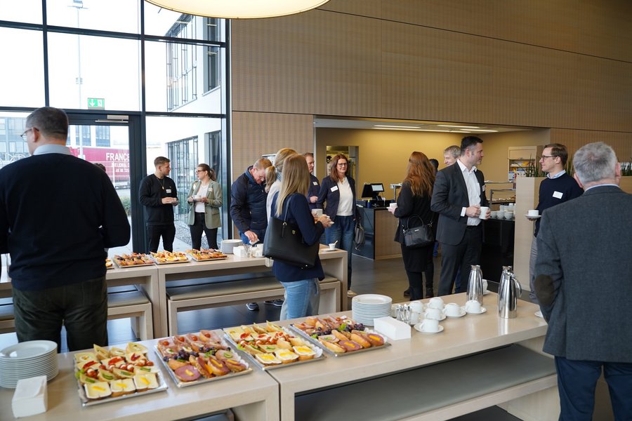 Mehrere Leute stehen an einem Frühstücksbuffet und unterhalten sich.