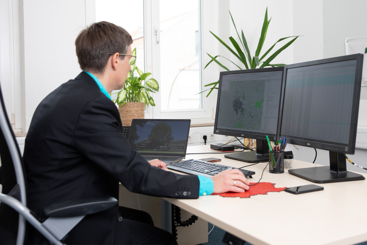 Ein Mann schaut an einem Arbeitsplatz auf zwei Monitore und ist am arbeiten.