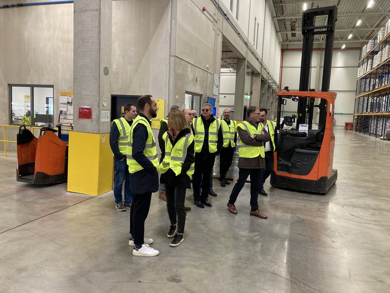 Eine Gruppe von Menschen in gelben Warnwesten geht durch eine moderne Produktionshalle.