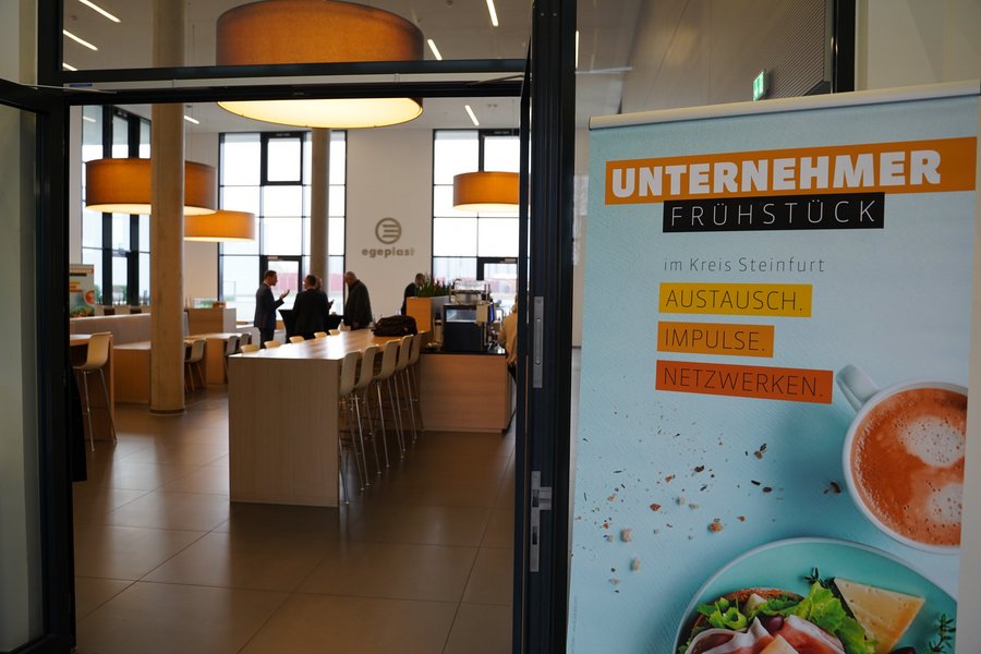 Ein Rollup mit der Aufschrift "Unternehmerfrühstück" steht vor dem Eingang eines modernen Foyers.
